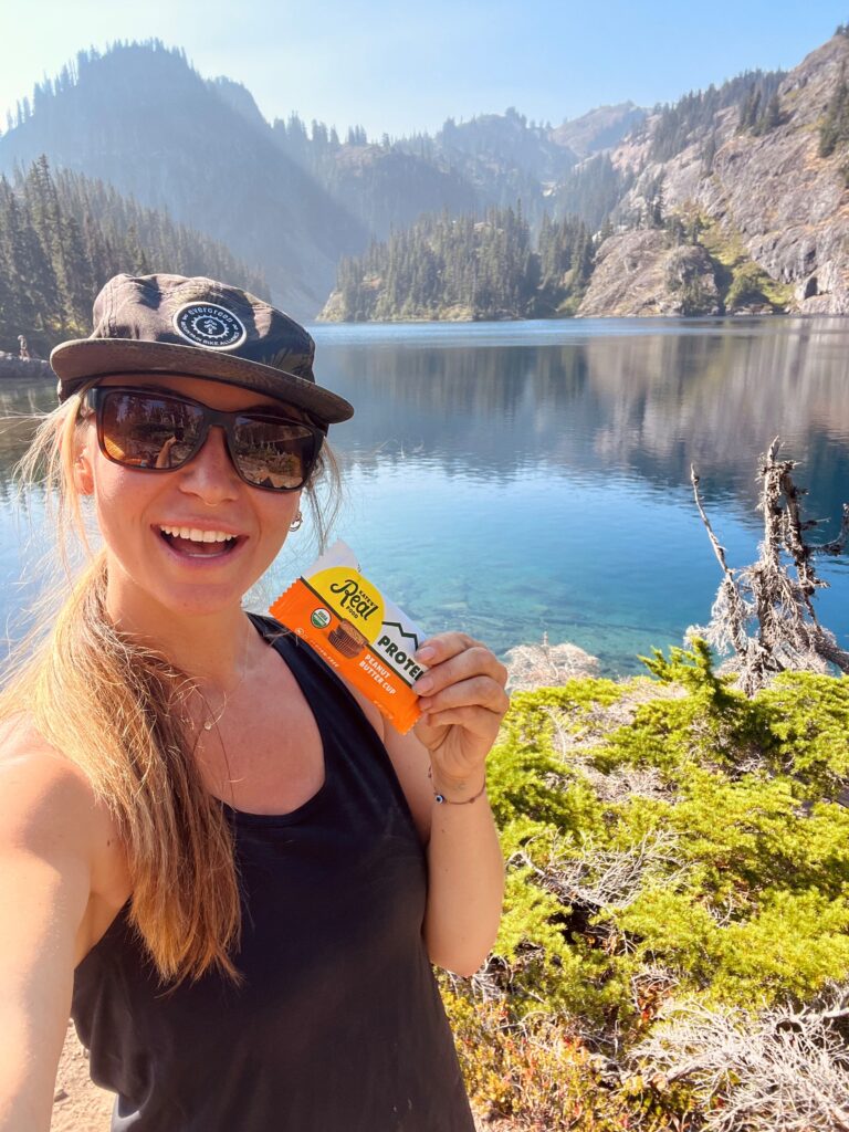 A woman at a mountain lake enjoying the outdoors—Kate’s Real Food’s adventure-driven ethos